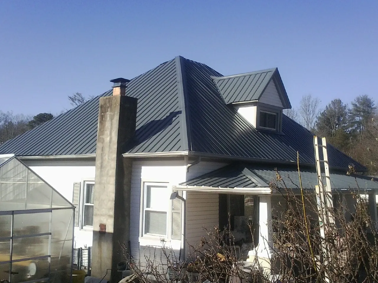 Dark blue standing seam metal roof on a white farmhouse with dormer — Slate & Tile Roof Repair by Roofing Brothers in Park Hall