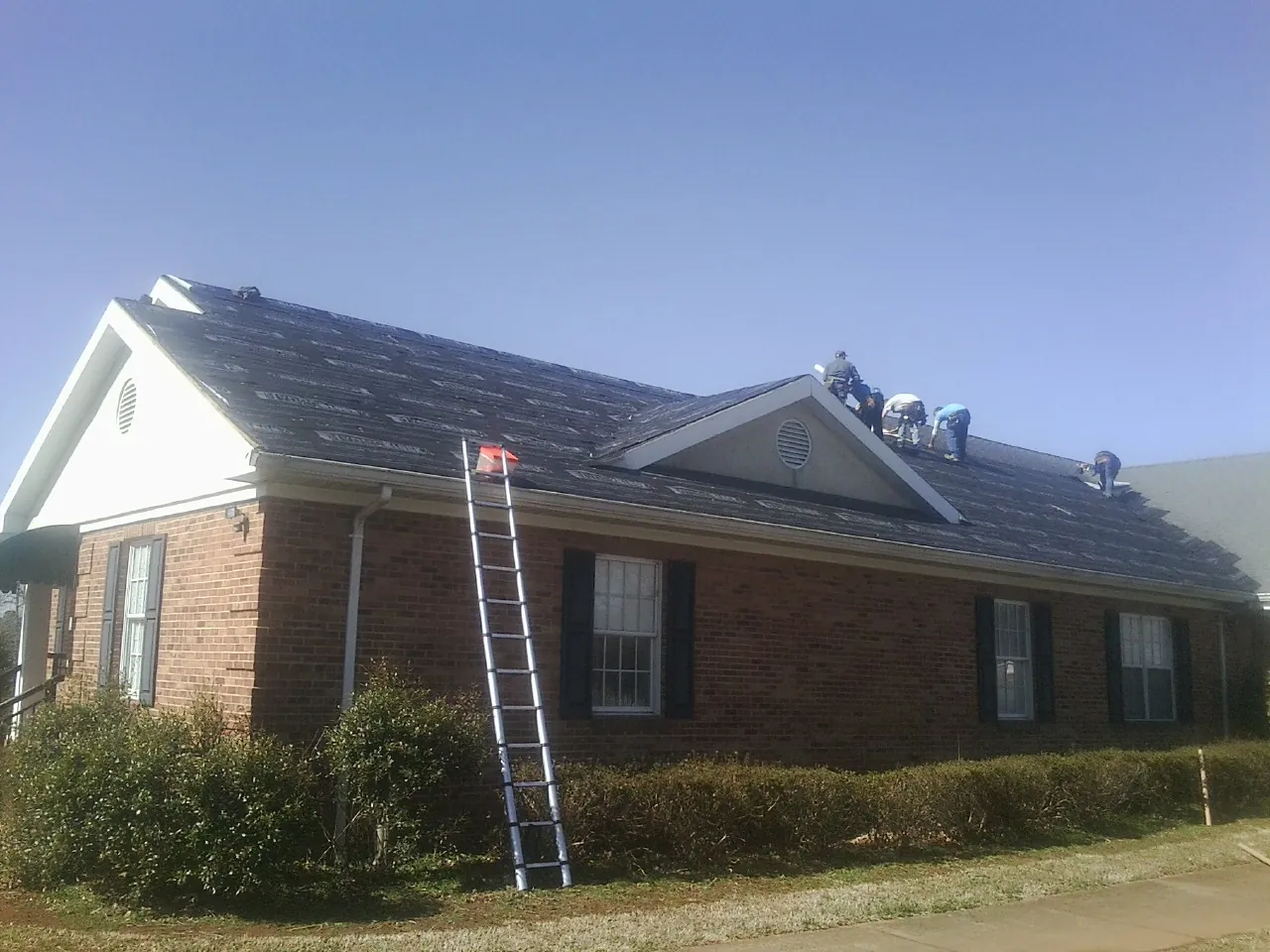 Crew tearing shingles off a brick ranch roof with a ladder set — Metal Roof Repair work by our crew in Park Hall