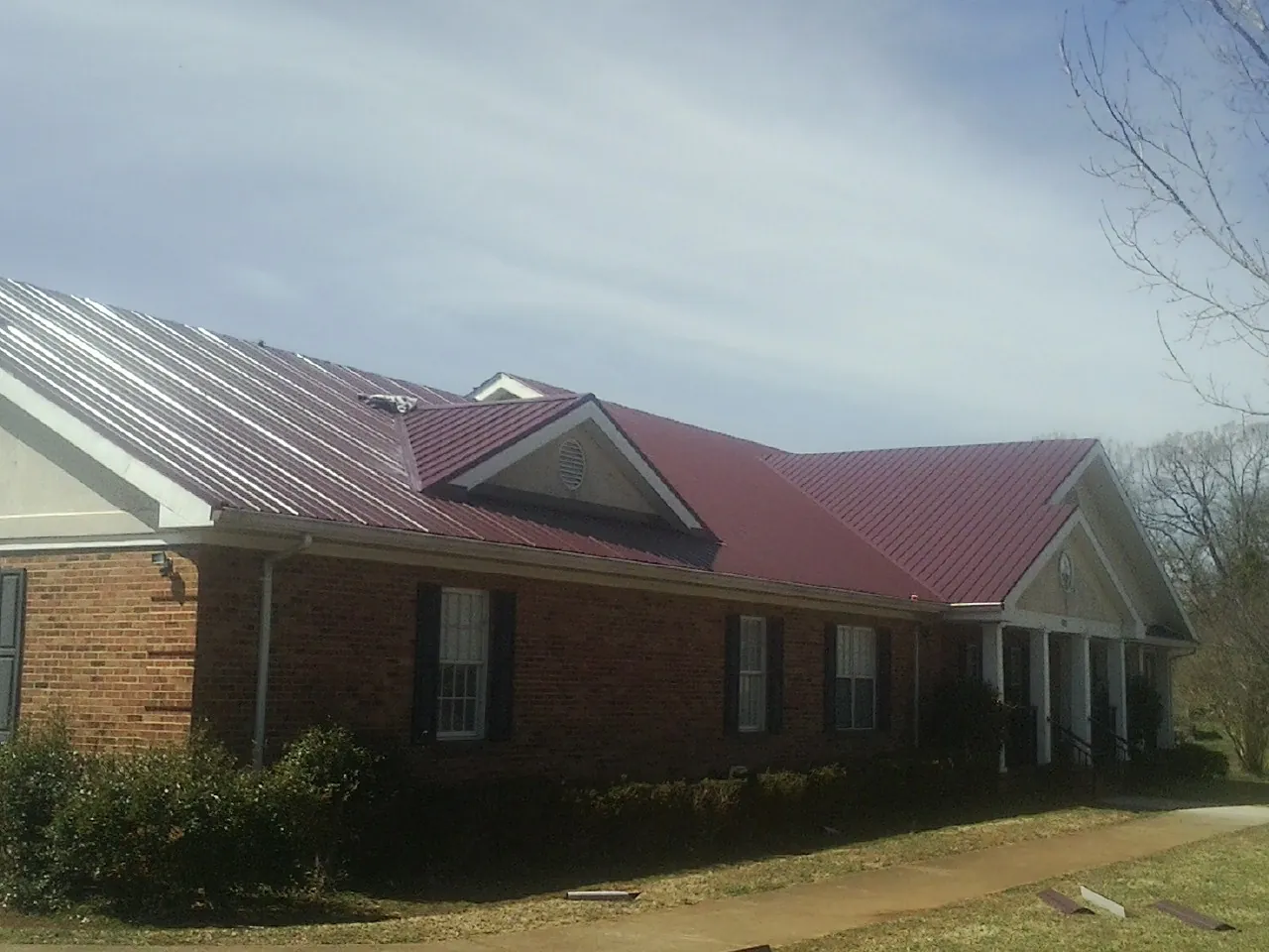 Red metal roof with gabled entries on a long brick building, from a Hail Damage Roof Repair job in Park Hall