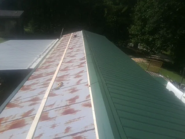 Old rusted panels beside newly installed green metal roofing — Wind Damage Roof Repair by Roofing Brothers in Park Hall