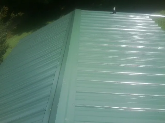New green metal panels meeting at the ridge of a roof — Flat Roof Repair work by our crew in Park Hall