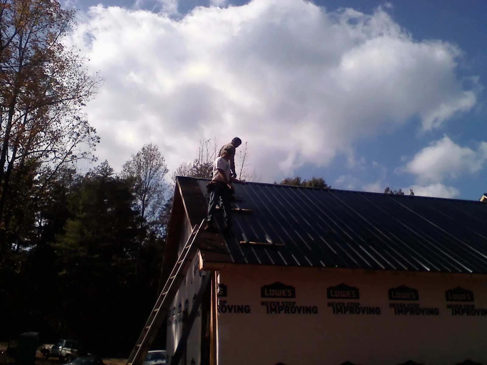 Roofer fastening dark metal panels high against a cloudy sky, from a Roof Inspection job in Park Hall
