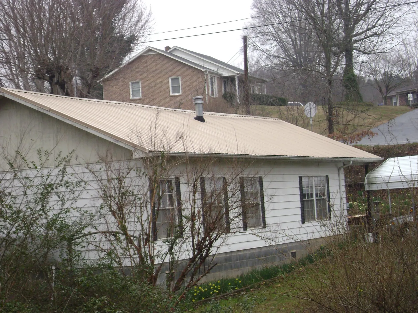 Tan metal roof on a white sided house set into a hillside — Commercial Roofing by Roofing Brothers in Park Hall