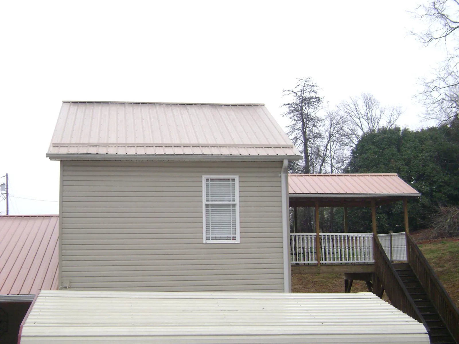 Tan metal roofs on a two story addition and attached porch, from a Roof Replacement job in Park Hall